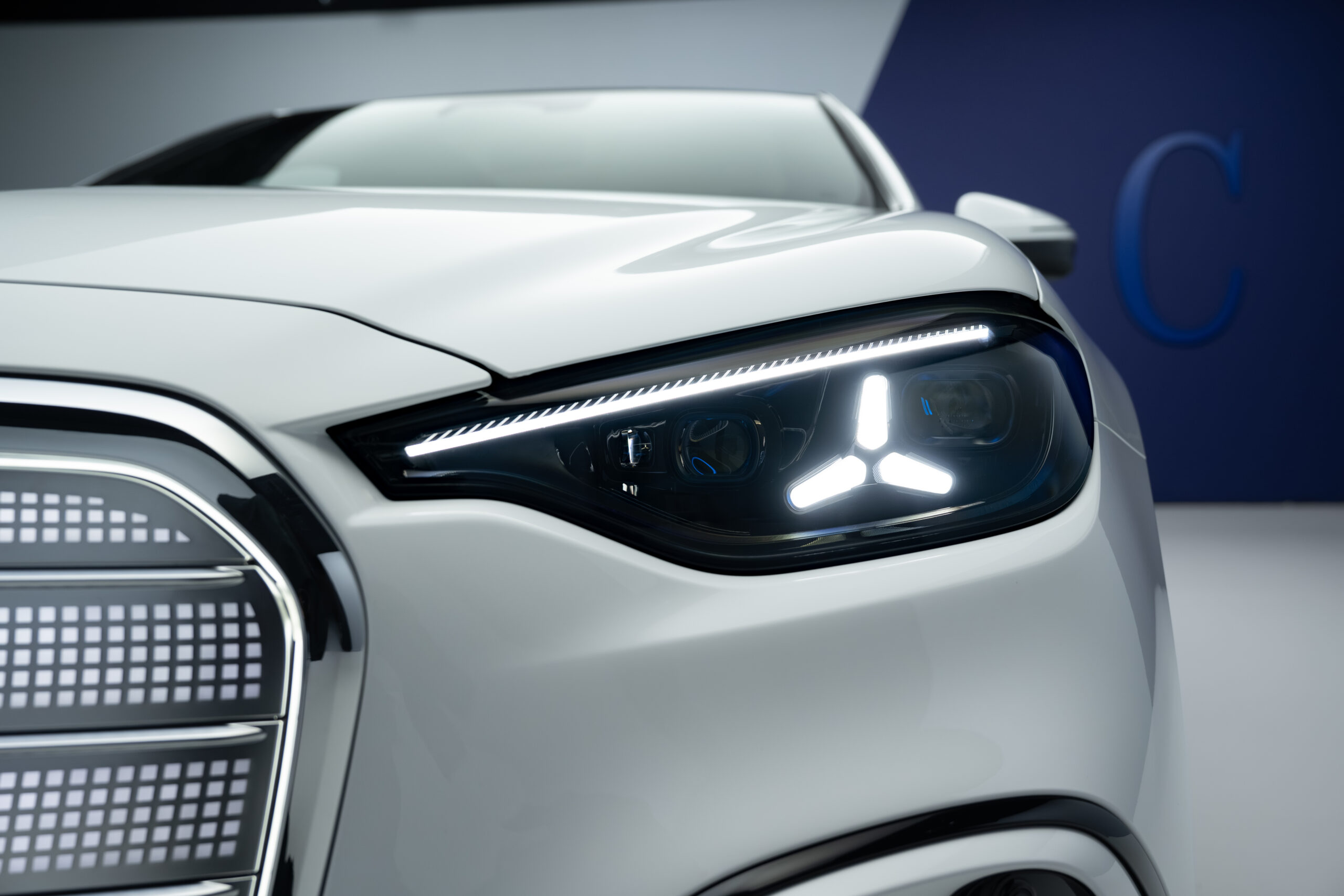 新型メルセデス・ベンツ電気Cクラス（2026年）フロントヘッドライト。三ツ星モチーフのLEDデイタイムランニングライトと上部LEDストリップが輝く
